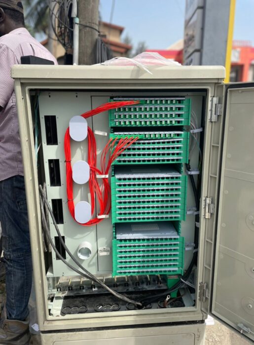Open roadside fibre distribution cabinet with green patch trays, coiled red jumpers and white cable spools