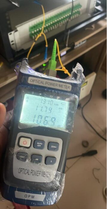 Handheld optical power meter reading 1310 nm connected to a green connector with a yellow fibre cable